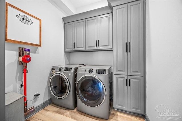 laundry area with cabinet space, light wood-style flooring, washing machine and dryer, and baseboards