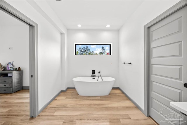 bathroom with a freestanding bath, recessed lighting, baseboards, and wood finished floors