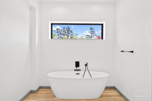 bathroom with a freestanding bath, wood finished floors, and a healthy amount of sunlight