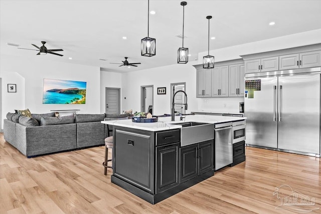 kitchen with light wood-type flooring, open floor plan, ceiling fan, stainless steel appliances, and a sink