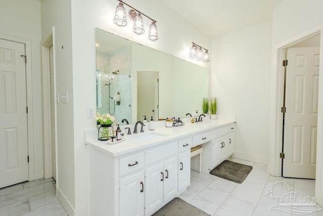 full bath with marble finish floor, a sink, a shower stall, double vanity, and baseboards