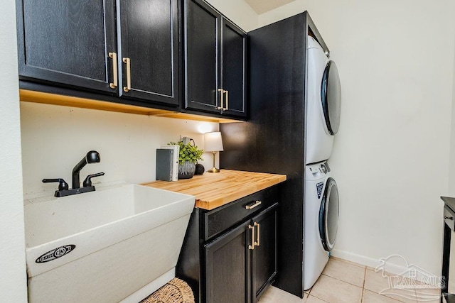 laundry area featuring a sink, cabinet space, stacked washer / dryer, light tile patterned floors, and baseboards