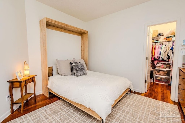 bedroom featuring a spacious closet, wood finished floors, a closet, and baseboards