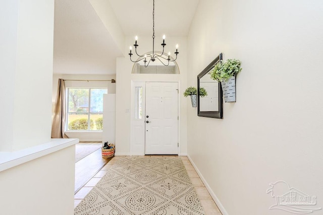 entryway with a notable chandelier, light tile patterned floors, and baseboards