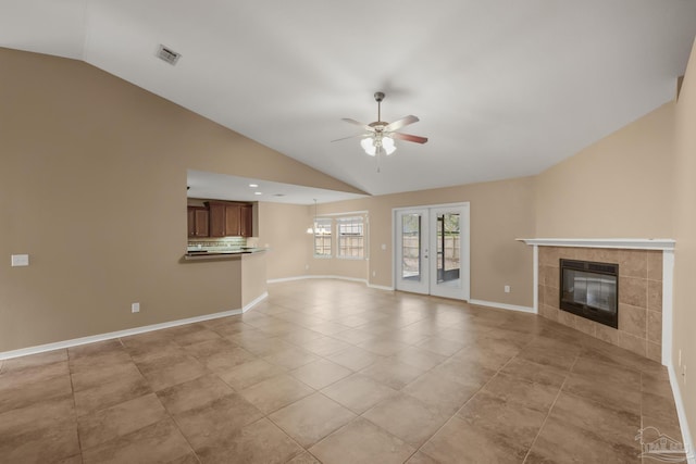 unfurnished living room featuring vaulted ceiling, a fireplace, light tile patterned floors, ceiling fan, and french doors