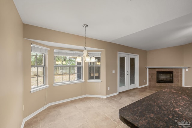 unfurnished living room featuring a tiled fireplace, light tile patterned flooring, a chandelier, and french doors