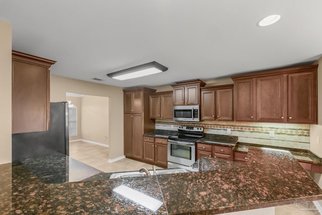 kitchen with stainless steel appliances, backsplash, dark stone counters, and kitchen peninsula