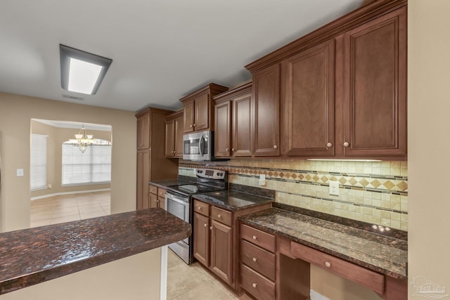 kitchen featuring dark stone countertops, appliances with stainless steel finishes, decorative backsplash, and a notable chandelier