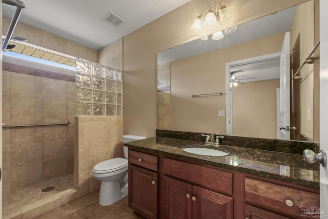 bathroom with ceiling fan, tile patterned flooring, tiled shower, vanity, and toilet