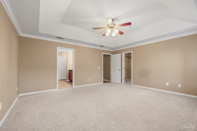 unfurnished bedroom with connected bathroom, a spacious closet, ornamental molding, a tray ceiling, and light colored carpet