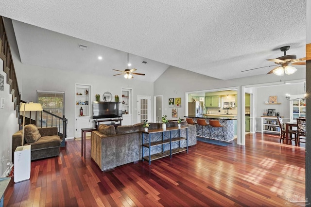 living room featuring built in shelves, vaulted ceiling, a textured ceiling, dark hardwood / wood-style flooring, and ceiling fan