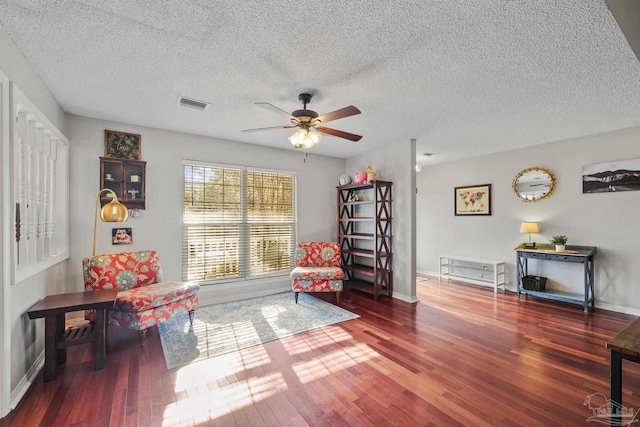 living area with dark wood-type flooring, a textured ceiling, and ceiling fan