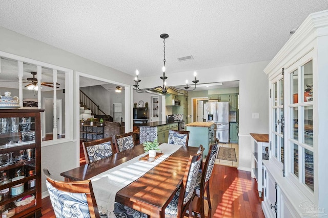 dining room with dark hardwood / wood-style flooring, ceiling fan with notable chandelier, and a textured ceiling