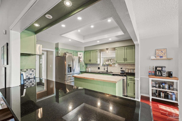 kitchen with butcher block counters, green cabinetry, appliances with stainless steel finishes, a raised ceiling, and decorative backsplash