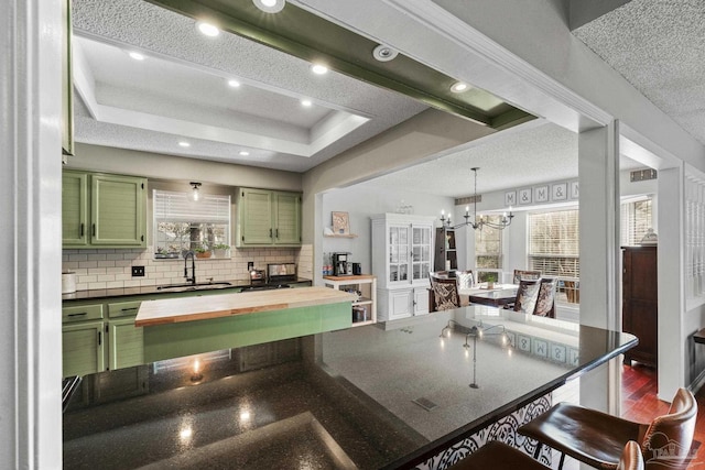 kitchen with sink, a tray ceiling, green cabinetry, and backsplash