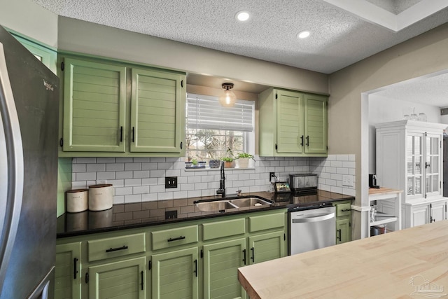 kitchen featuring sink, backsplash, stainless steel appliances, green cabinetry, and a textured ceiling