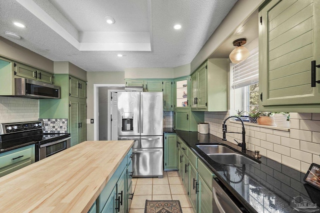 kitchen with sink, butcher block countertops, a tray ceiling, green cabinets, and stainless steel appliances