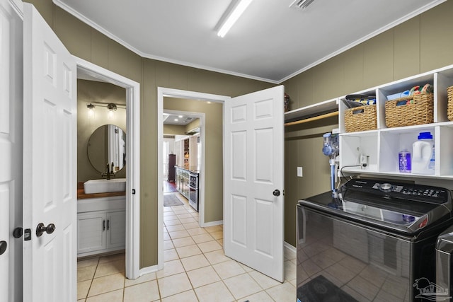 clothes washing area with crown molding, sink, light tile patterned floors, and washing machine and dryer