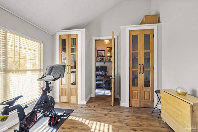 exercise area featuring lofted ceiling, hardwood / wood-style floors, french doors, and a textured ceiling