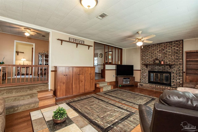 living room featuring ceiling fan, a brick fireplace, crown molding, hardwood / wood-style floors, and wooden walls