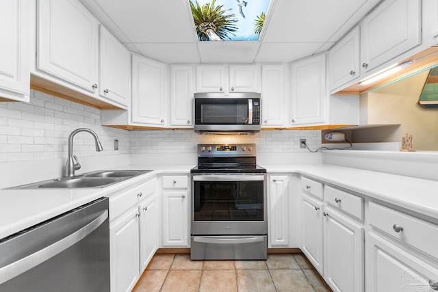 kitchen with appliances with stainless steel finishes, backsplash, white cabinets, light tile patterned floors, and sink