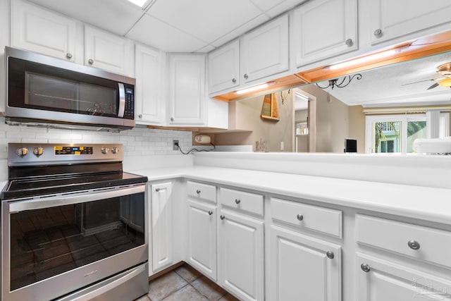 kitchen with appliances with stainless steel finishes, light tile patterned flooring, decorative backsplash, and white cabinetry