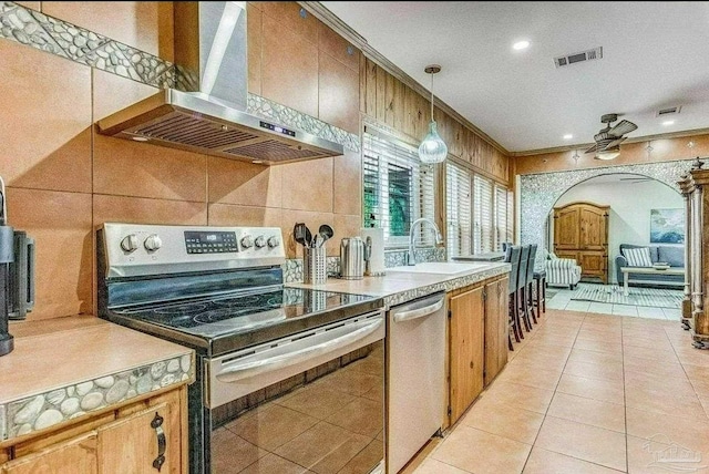 kitchen with pendant lighting, sink, crown molding, stainless steel appliances, and exhaust hood