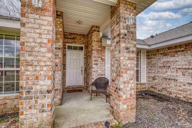 view of exterior entry with covered porch, brick siding, and a shingled roof