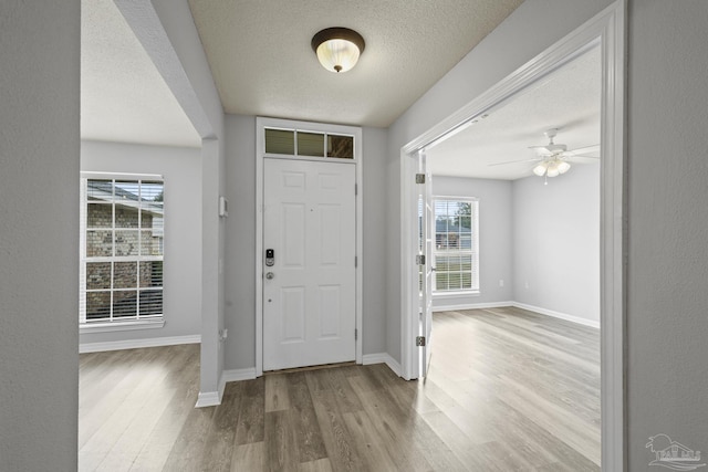 foyer entrance with ceiling fan, a textured ceiling, baseboards, and wood finished floors