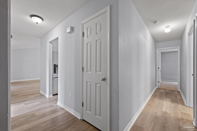 corridor featuring light wood-type flooring, a textured ceiling, and baseboards