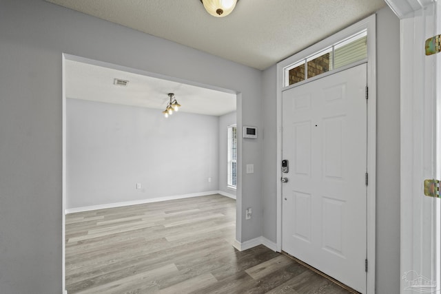 entryway with baseboards, a textured ceiling, visible vents, and wood finished floors