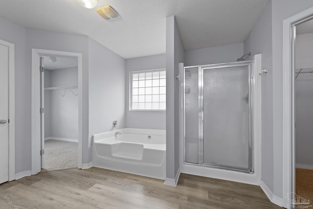 full bath with a walk in closet, a shower stall, a textured ceiling, wood finished floors, and a bath