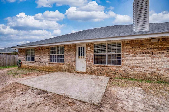 back of property featuring brick siding, a shingled roof, fence, a chimney, and a patio area