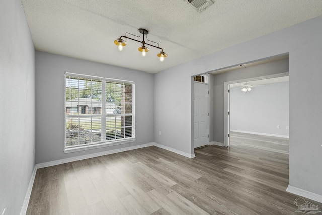 empty room featuring visible vents, ceiling fan, a textured ceiling, wood finished floors, and baseboards