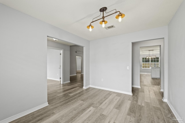 unfurnished room with visible vents, a notable chandelier, baseboards, and wood finished floors