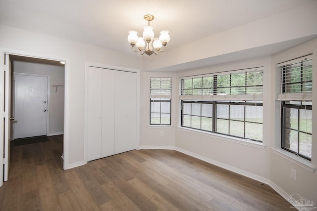 unfurnished bedroom featuring a closet, a chandelier, dark wood-style flooring, and baseboards