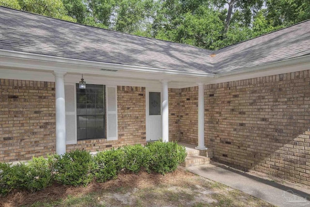 entrance to property featuring brick siding, roof with shingles, and covered porch
