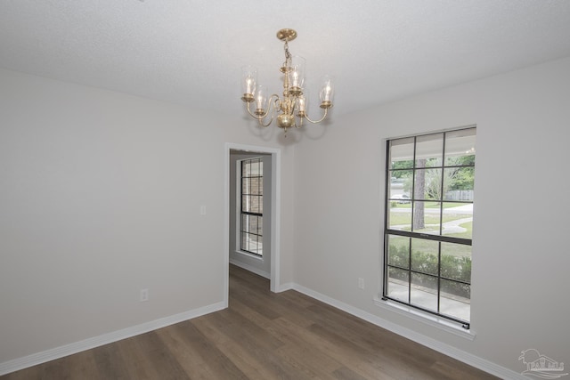 unfurnished room with baseboards, dark wood-style flooring, and an inviting chandelier