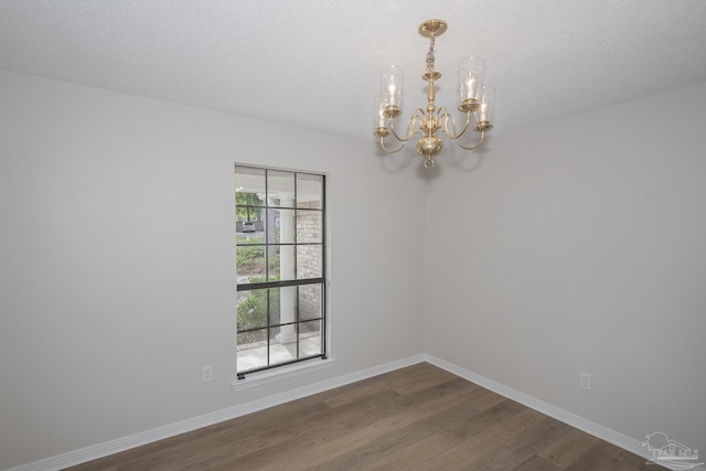 unfurnished room featuring dark wood-style flooring, a notable chandelier, and baseboards