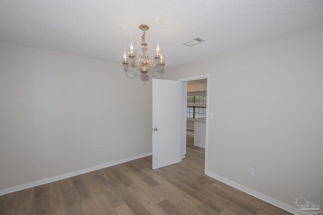 unfurnished room featuring visible vents, wood finished floors, baseboards, and a notable chandelier