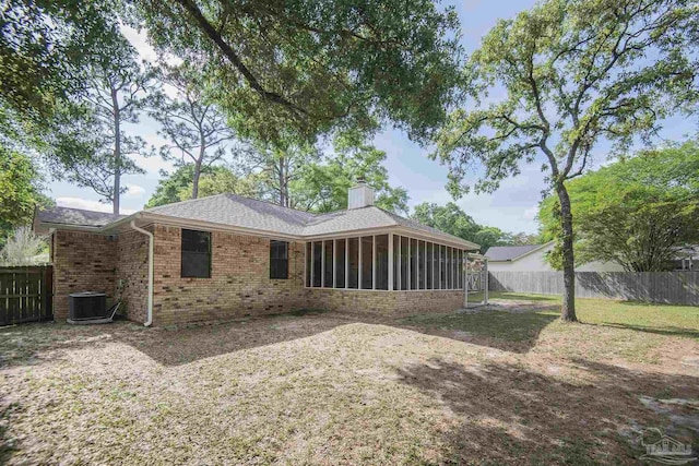 rear view of house featuring a chimney, brick siding, a sunroom, and a fenced backyard