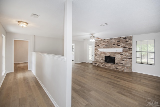 unfurnished living room featuring a fireplace, a ceiling fan, visible vents, and wood finished floors