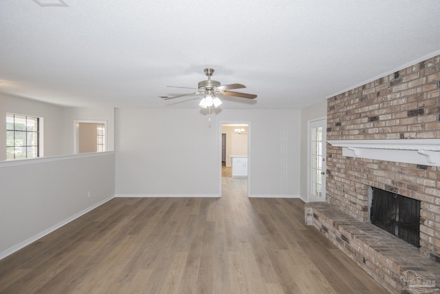 unfurnished living room featuring a ceiling fan, a textured ceiling, baseboards, a brick fireplace, and wood finished floors
