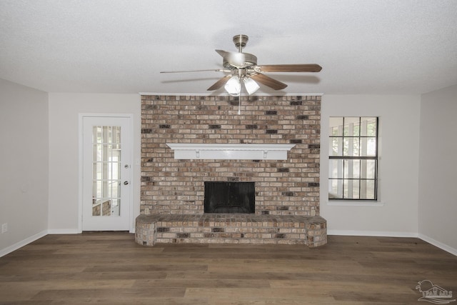 unfurnished living room with wood finished floors, a textured ceiling, a fireplace, a ceiling fan, and baseboards