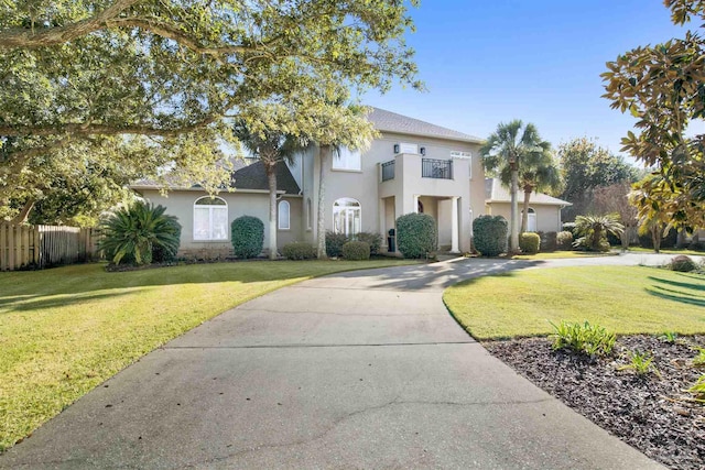 view of front facade with a balcony, fence, concrete driveway, stucco siding, and a front lawn