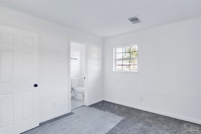 unfurnished bedroom featuring dark carpet and ensuite bath