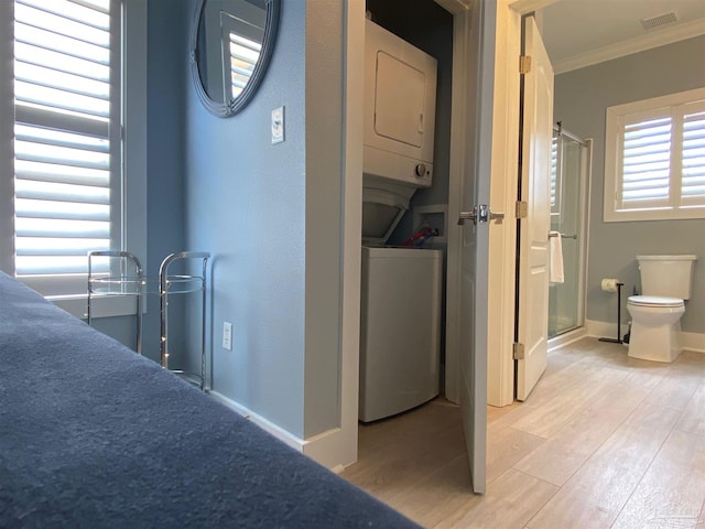 clothes washing area featuring crown molding, stacked washer and clothes dryer, and light wood-type flooring