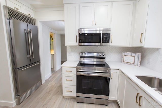kitchen with tasteful backsplash, white cabinetry, stainless steel appliances, light wood-style floors, and light countertops