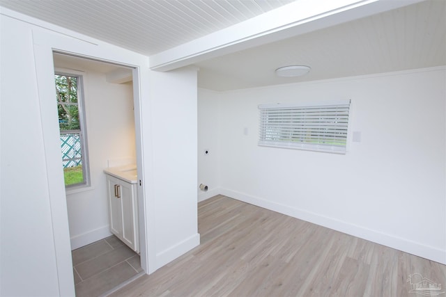 spare room with beam ceiling, light wood-type flooring, and baseboards