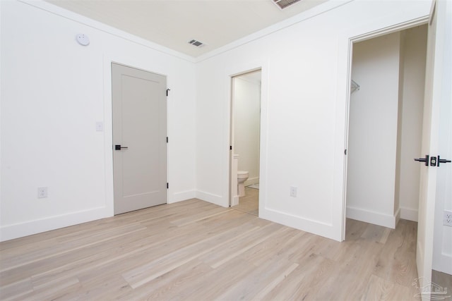 unfurnished bedroom featuring crown molding, light hardwood / wood-style flooring, ensuite bath, and a closet